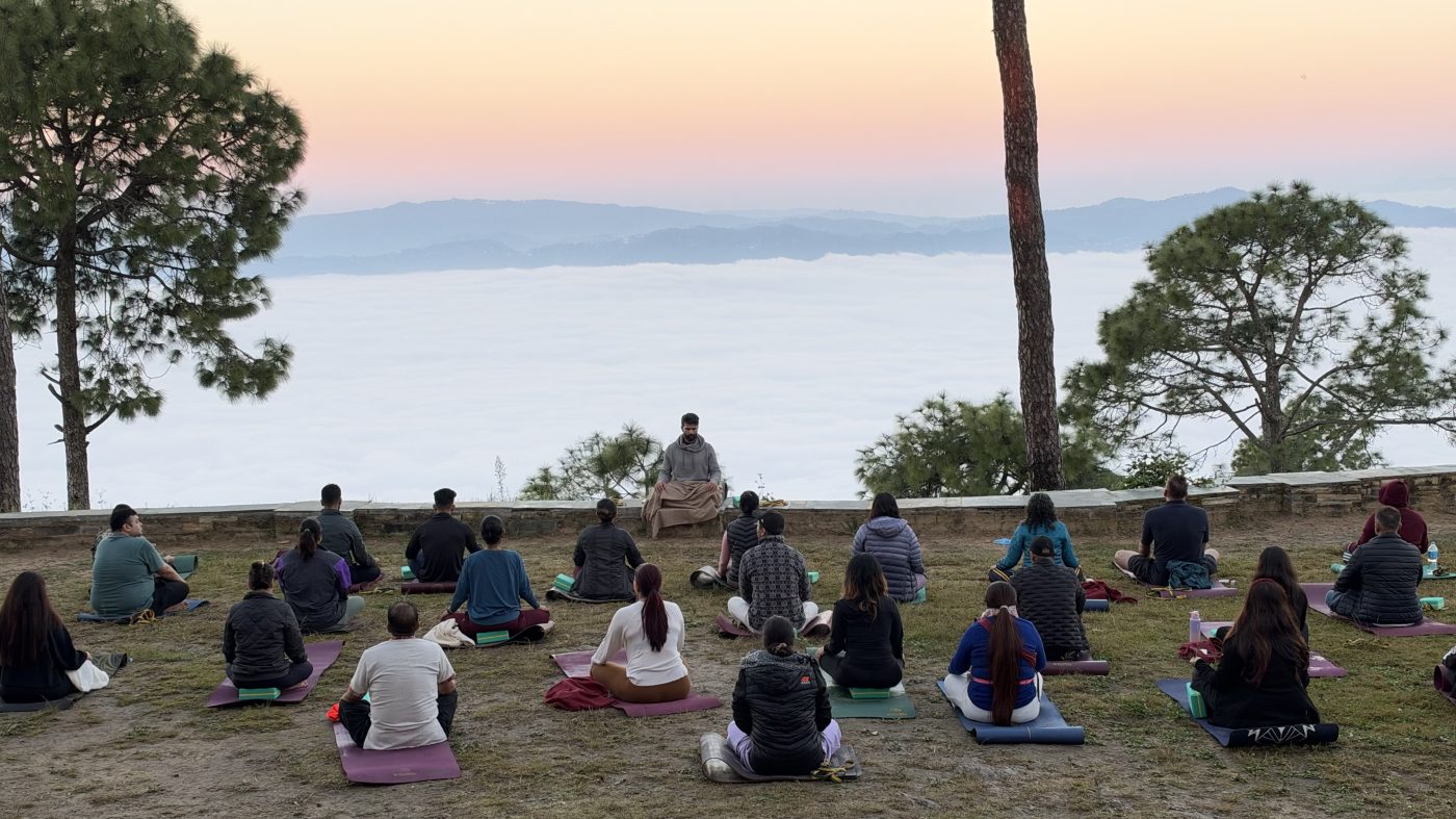 A group meditating together above the valley at sunset